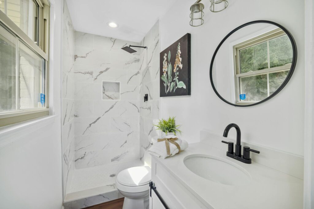 Sleek bathroom featuring marble shower, round mirror, and contemporary fixtures.